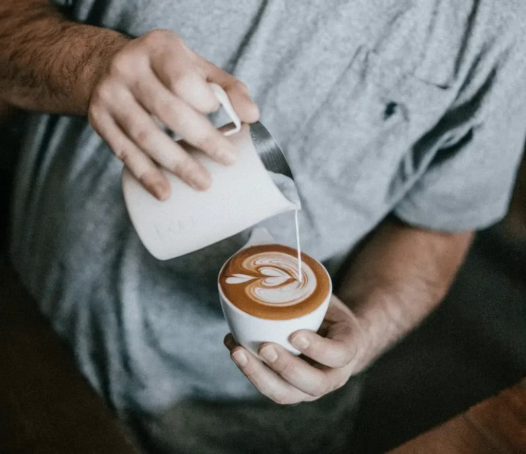 someone pouring milk into a coffee cup with a latte art design