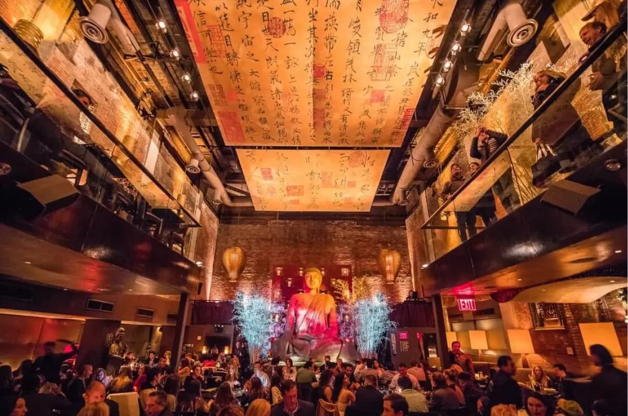a large venue with a buda statue in the background and a group of people sitting at tables and having dinner