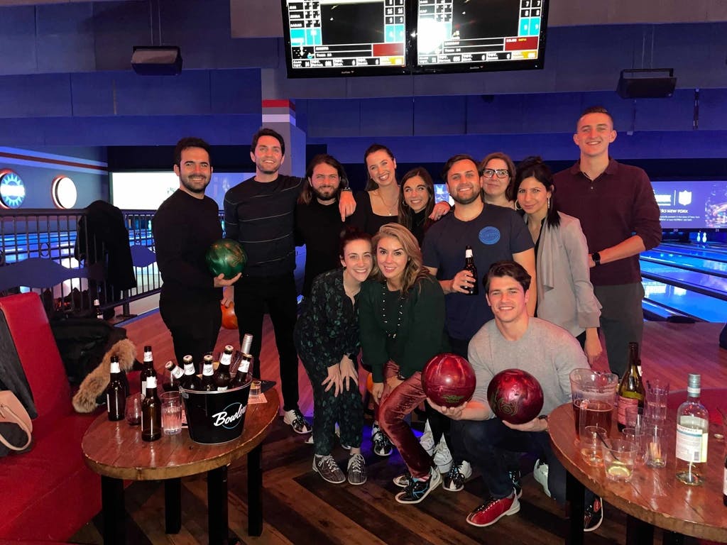 a group of people at a bowling alley with bowling balls, smiling and looking at the camera