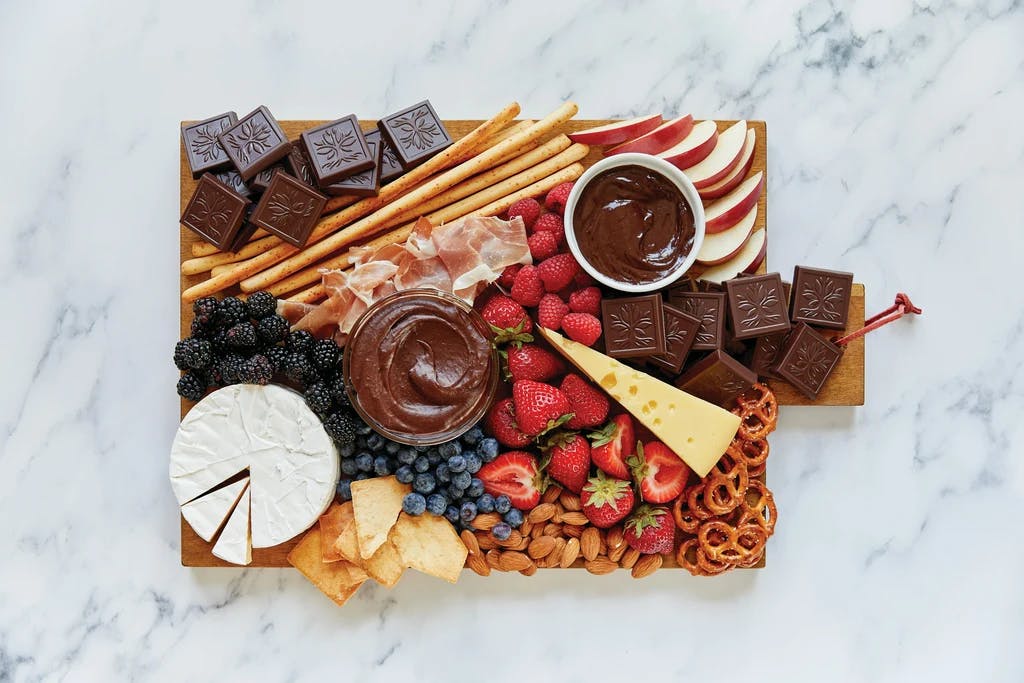 a charcuterie board with different meats, cheeses, fruite, and chocolate