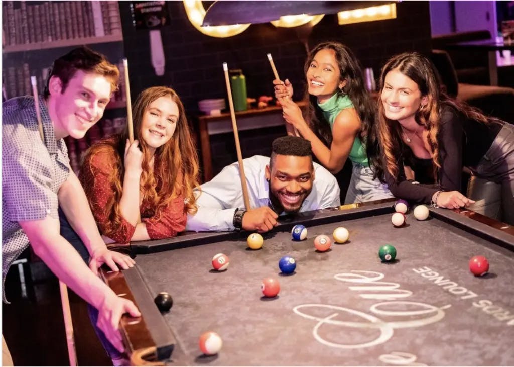 a group of people at a pool table smiling at the camera