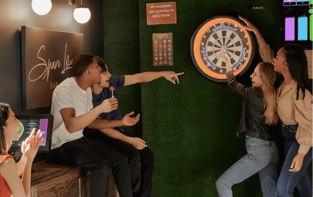 a group of people around a dart board throwing darts and laughing