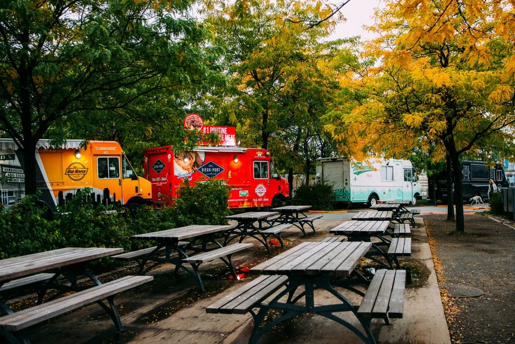 a set of picnic tables in a park with a line of food trucks behind them