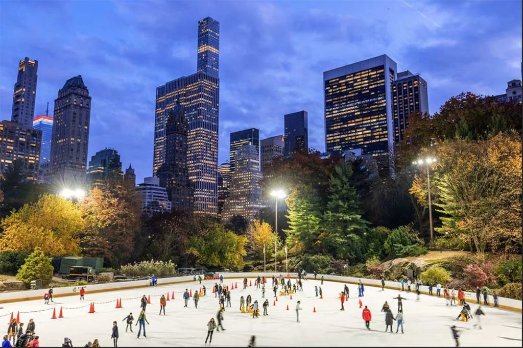 people ice skating at a rink in central park with building in the background