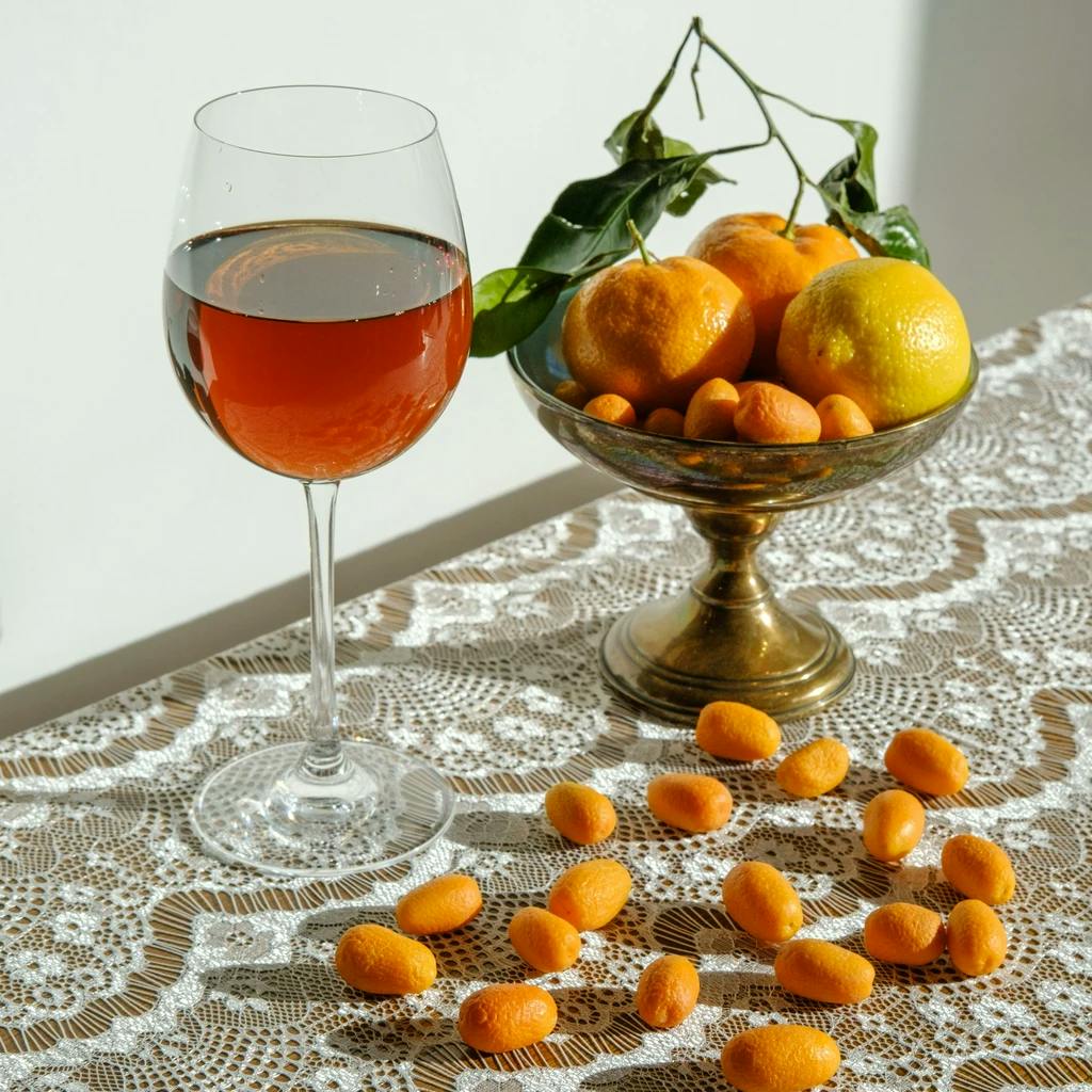 a glass of orange wine on a table with oranges around it