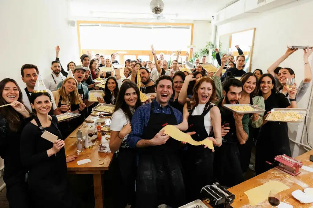 a large group of people, smiling and showing the pizza they made