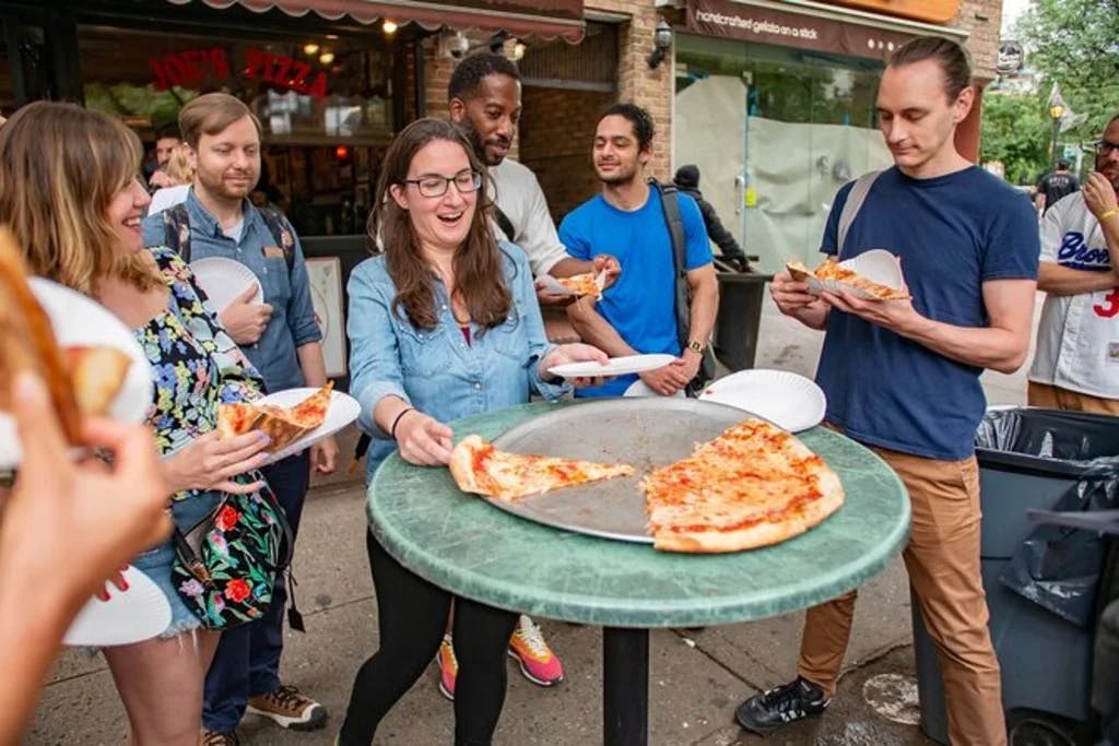 a group of poeple standing around and outdoor table having pizza