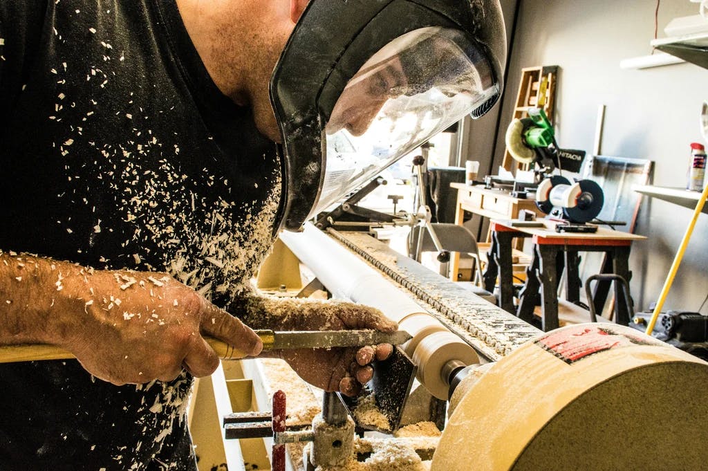 somone shaping wood on a machine and wearing a mask