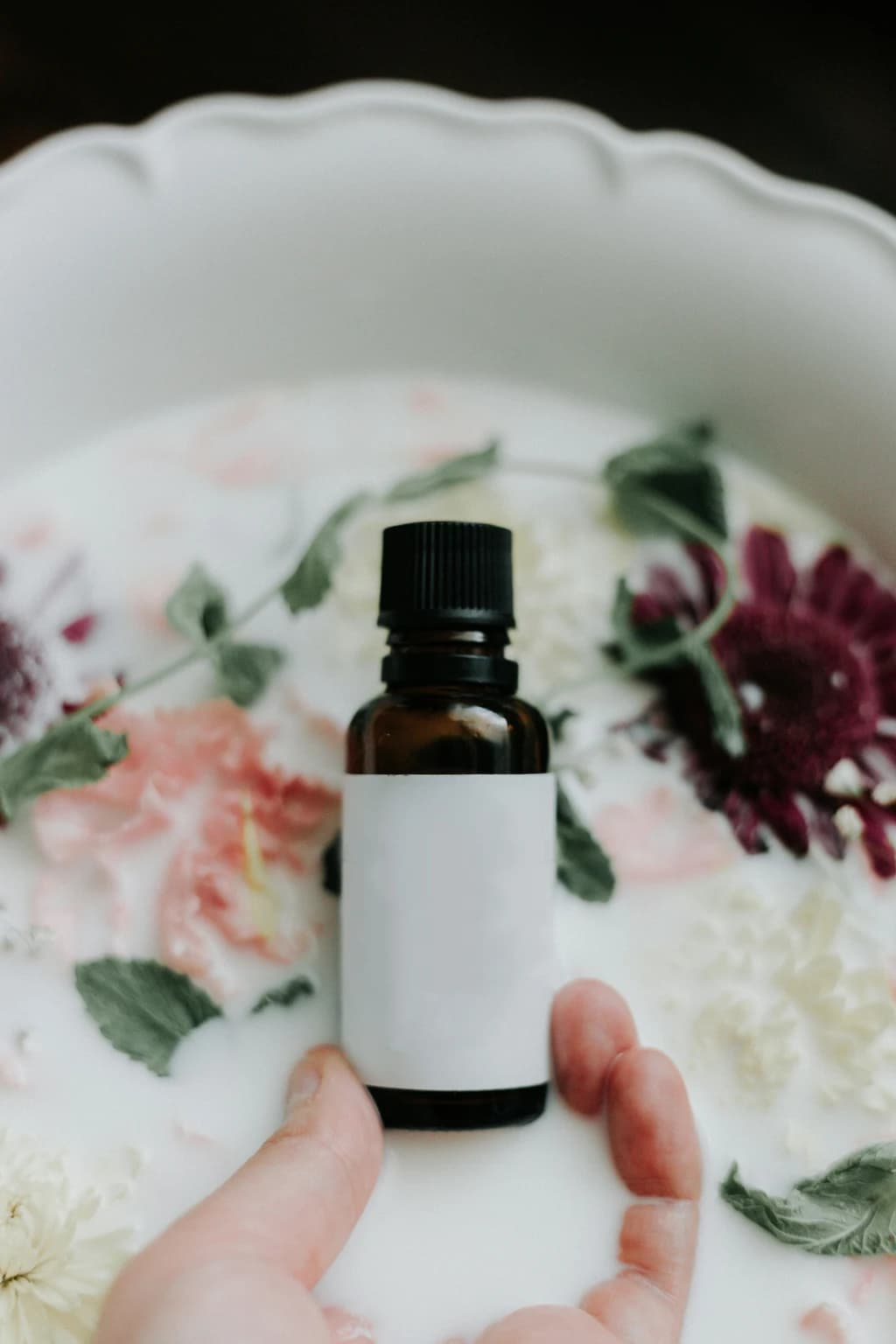 A brown bottle placed against a floral background in a white bowl filled with water, giving a spa-like atmosphere.