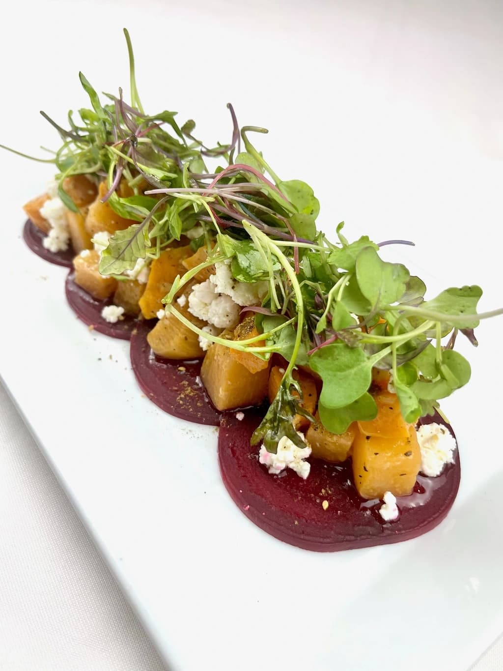 A vibrant salad with roasted golden beets, crumbled feta cheese, and microgreens, artistically arranged on a white plate with beet puree.