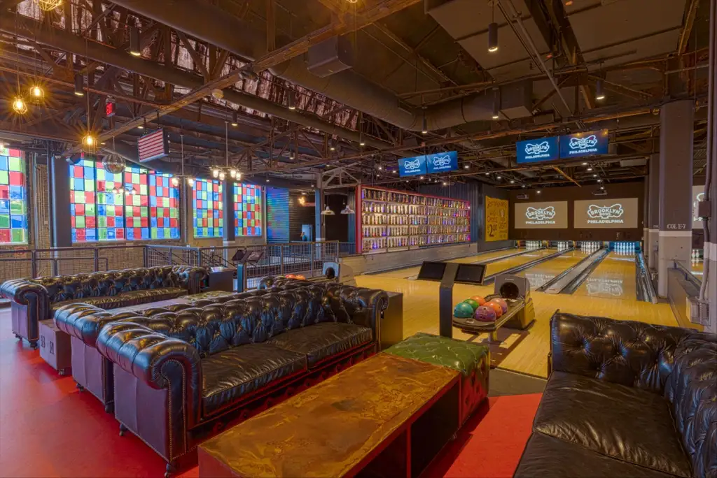 Stylish bowling alley with leather couches, colorful stained-glass windows, and multiple lanes, creating a chic and relaxed atmosphere.