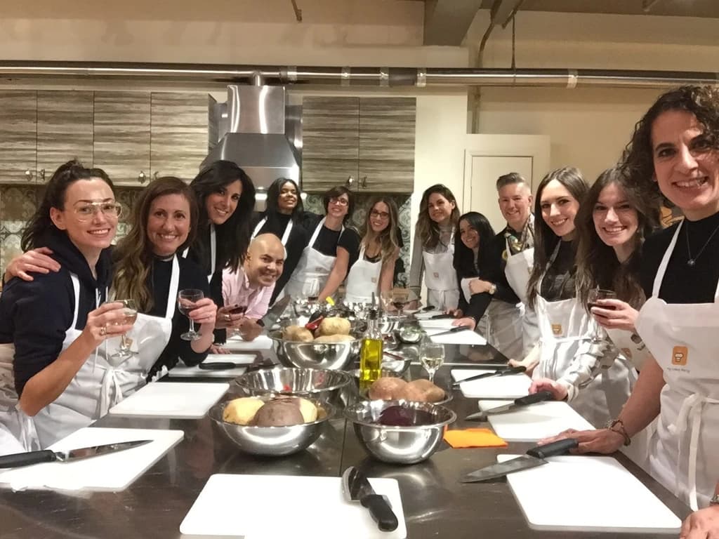 A cheerful group of people wearing aprons and standing around a kitchen counter, ready for a cooking class.