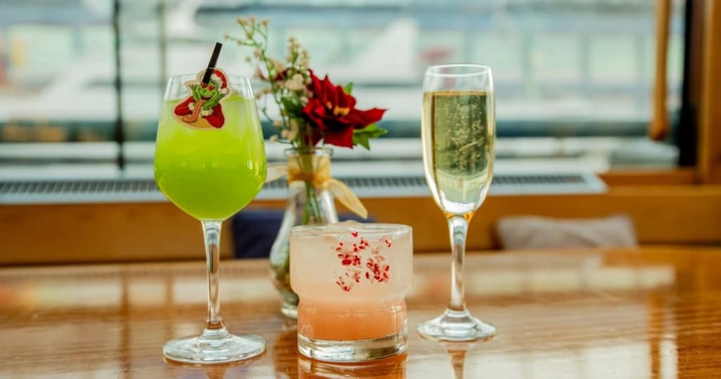 Three holiday-themed cocktails, including a bright green Grinch drink, on a wooden table with festive decorations.
