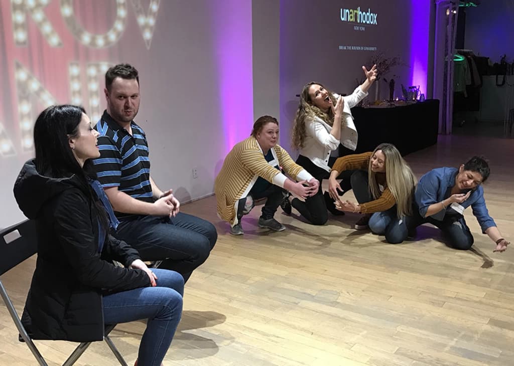 A group of five people posing dramatically on stage, each making different facial expressions and gestures during a fun improv activity.