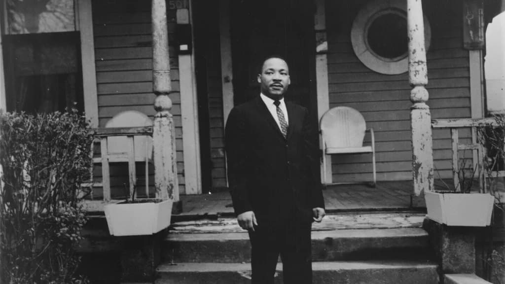 A black-and-white image of Dr. Martin Luther King Jr. standing confidently on the porch of his childhood home.