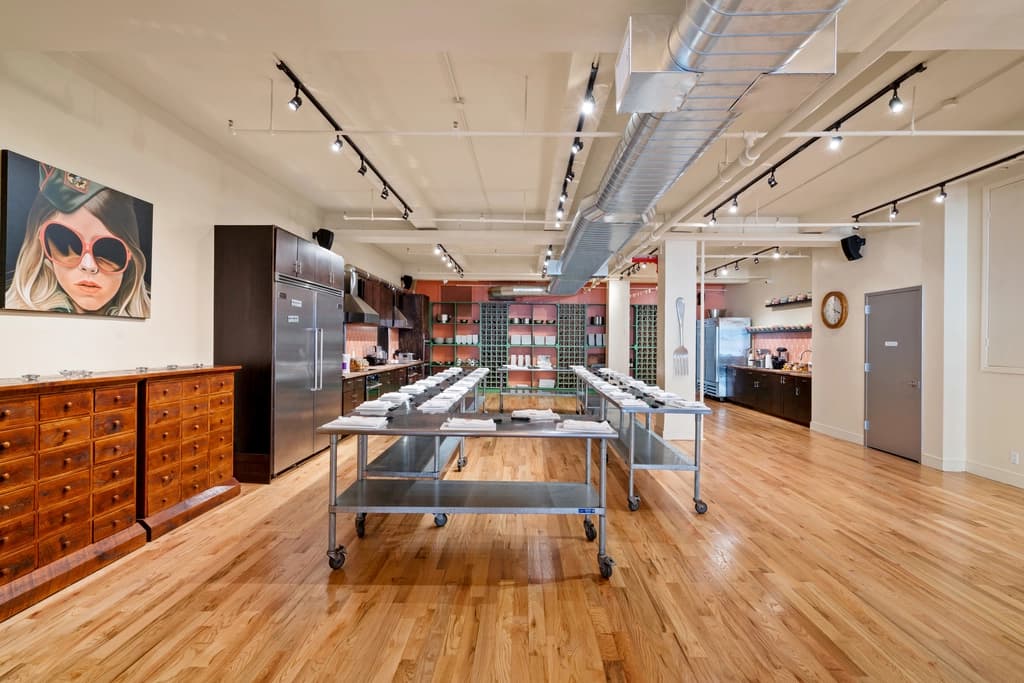 A spacious cooking studio with wooden floors, well-organized cooking stations, and artistic decorations, ready for a cooking class.