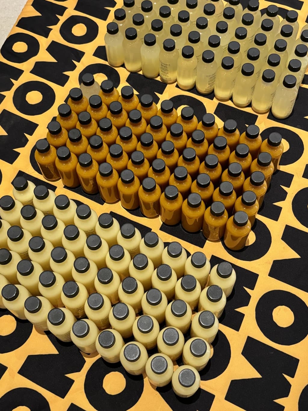 A colorful display of wellness shot bottles on a table with black caps and neatly arranged lines under bright lighting.